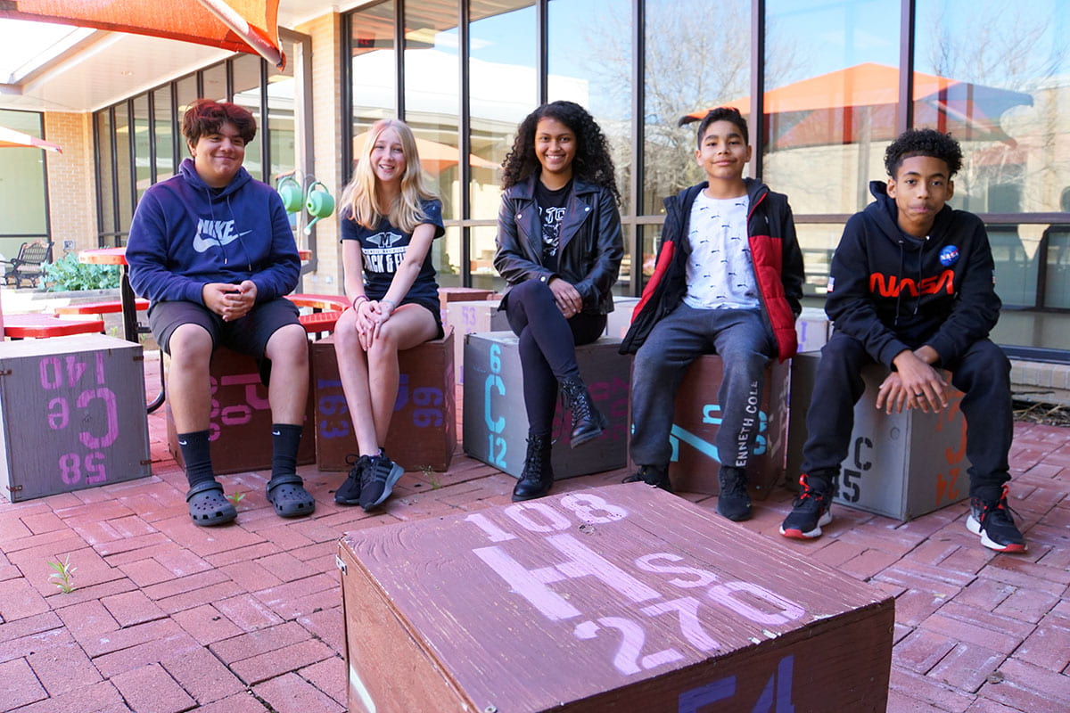 Five Chisholm Trail students posing for a photo in the courtyard, sitting on painted blocks