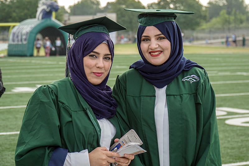 Two graduates from Mcneil high school posing for pictures in the graduation cap and gowns