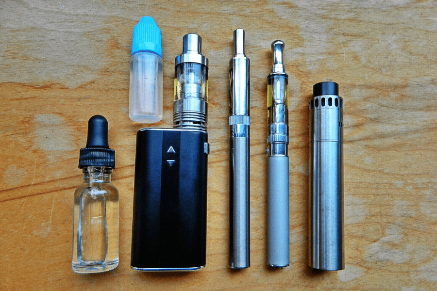 Various vape and e-cigarette devices laid flat on a wooden tabletop
