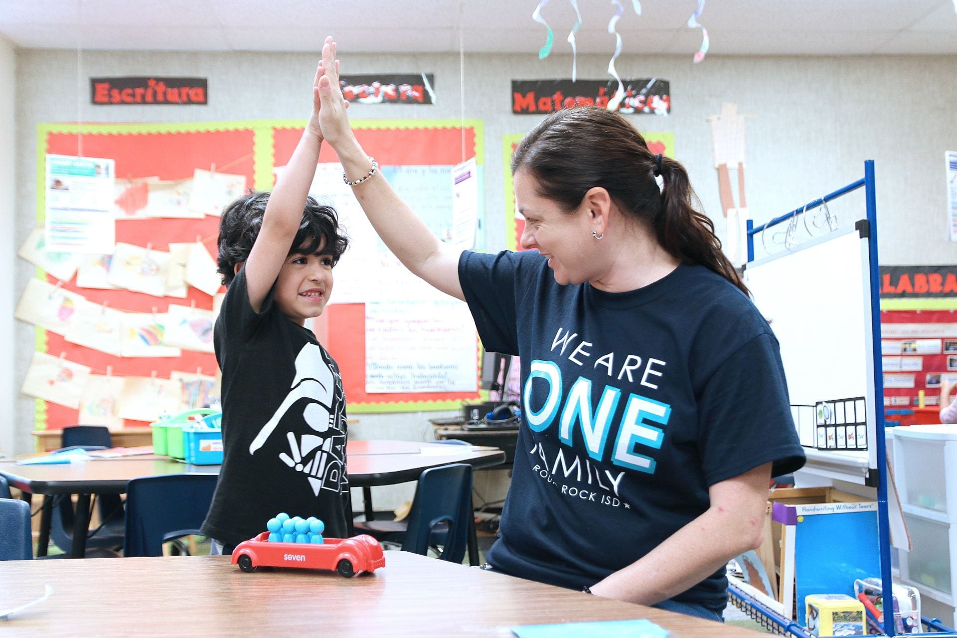 A PreK student and teacher give each other high fives.