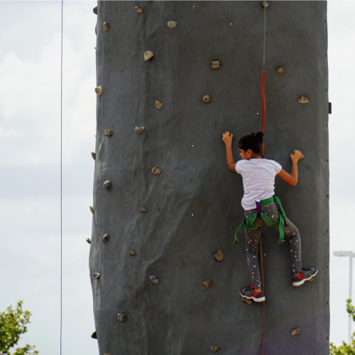 Child wearing a safety harness while climbing up a rock wall.